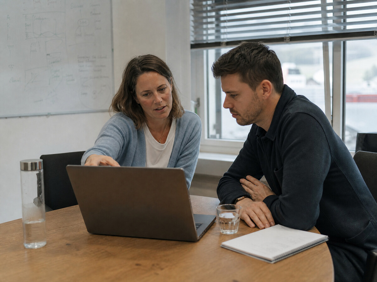 Zwei Kolleginnen und Kollegen besprechen sich an einem Laptop während eines kurzen Workshops in einem Schweizer KMU-Büro